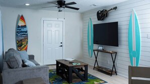 Een woonkamer met een grijze bank, een salontafel, een televisie en surfplanken aan de muur.