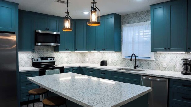 Een moderne keuken met blauwgroene kastjes, roestvrijstalen apparatuur en een centraal eiland met krukken.
