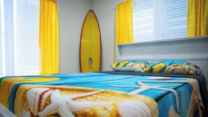 Een hotelkamer met een bed, versierd met een surfboard en beddengoed met een strandthema.