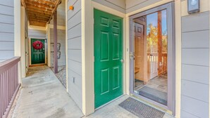 Une maison avec une porte verte, un porche doté d’un plafond en bois et une guirlande rouge accrochée à la porte.