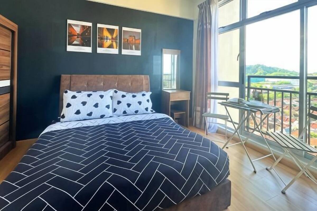 A bedroom with a large bed, a desk, and a balcony with a view.