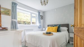 Une chambre à coucher avec un lit, une table de chevet, une fenêtre avec des rideaux, un radiateur et une porte.