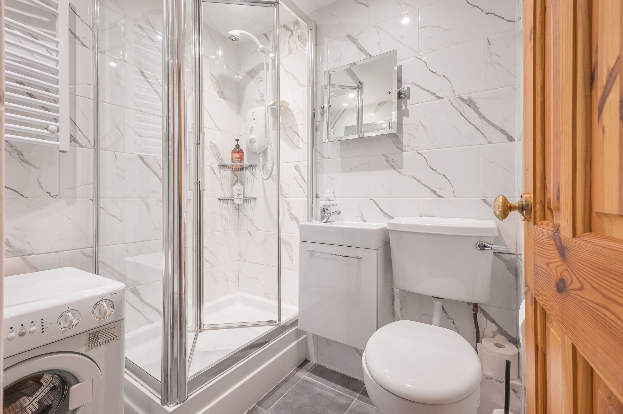 A modern bathroom with a glass-enclosed shower, a toilet, a sink, and a washing machine.