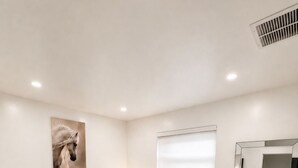 Ein Schlafzimmer mit einem großen Bett, einem Nachttisch mit Lampe, einem Wandspiegel und einem Gemälde eines Pferdes.
