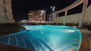 Une piscine dotée d’une terrasse carrelée et d’un bord incurvé, entourée d’une structure blanche agrémentée de colonnes.