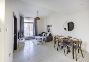 A modern living room with a sofa, coffee table, dining table with chairs, a hanging light fixture, and a large window with curtains. - Iconic Spacious 1br + Hall + 2 Baths In Mangroves Place Al-Reem Island Auh (Abu Dhabi)