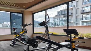 A gym with exercise equipment and large windows overlooking a cityscape.