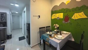 Un coin repas avec une table dressée pour deux personnes, un mur décoré d’une fresque verte et, au fond, un espace cuisine.