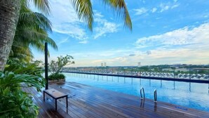 A wooden deck with a pool, palm trees, and a cityscape view. - ABHome [Camp Suite] Midas Seri Alam #Mall #JB (Plentong)