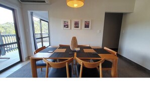 A dining area with a table set for four, wooden chairs, a central vase, and three framed pictures on the wall. - Paihia resort with all the amenities! (Paihia)