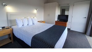 A hotel room with a bed, a TV, a wardrobe, and a door. - Paihia resort with all the amenities! (Paihia)