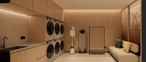A modern laundry room with a built-in washer and dryer, a sink, and a seating area with a sofa and pillows.