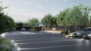 A modern hotel entrance with a paved driveway, two parked cars, and lush greenery. - Hilton Garden Inn  (Suzhou)