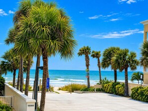 A coastal walkway lined with palm trees, leading to a beach with the ocean in the background. - Coastal Luxe  Pet-Friendly  Beach Private Balcony (Indian Rocks Beach)