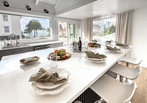 A modern kitchen with a long island, white countertops, and a view of the beach. - Coastal Luxe  Pet-Friendly  Beach Private Balcony (Indian Rocks Beach)