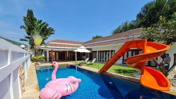 Una piscina con un flotador de flamenco rosa, un tobogán naranja y una zona de estar techada.