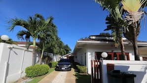 Una calle residencial con una casa, palmeras y un automóvil estacionado frente a ella.