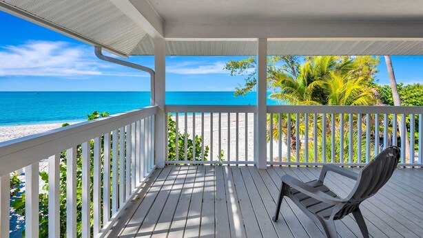 A wooden deck with a white railing overlooking a beach with clear blue water and palm trees. - 3BR Gulf-Front Luxury with Panoramic Views (Englewood)