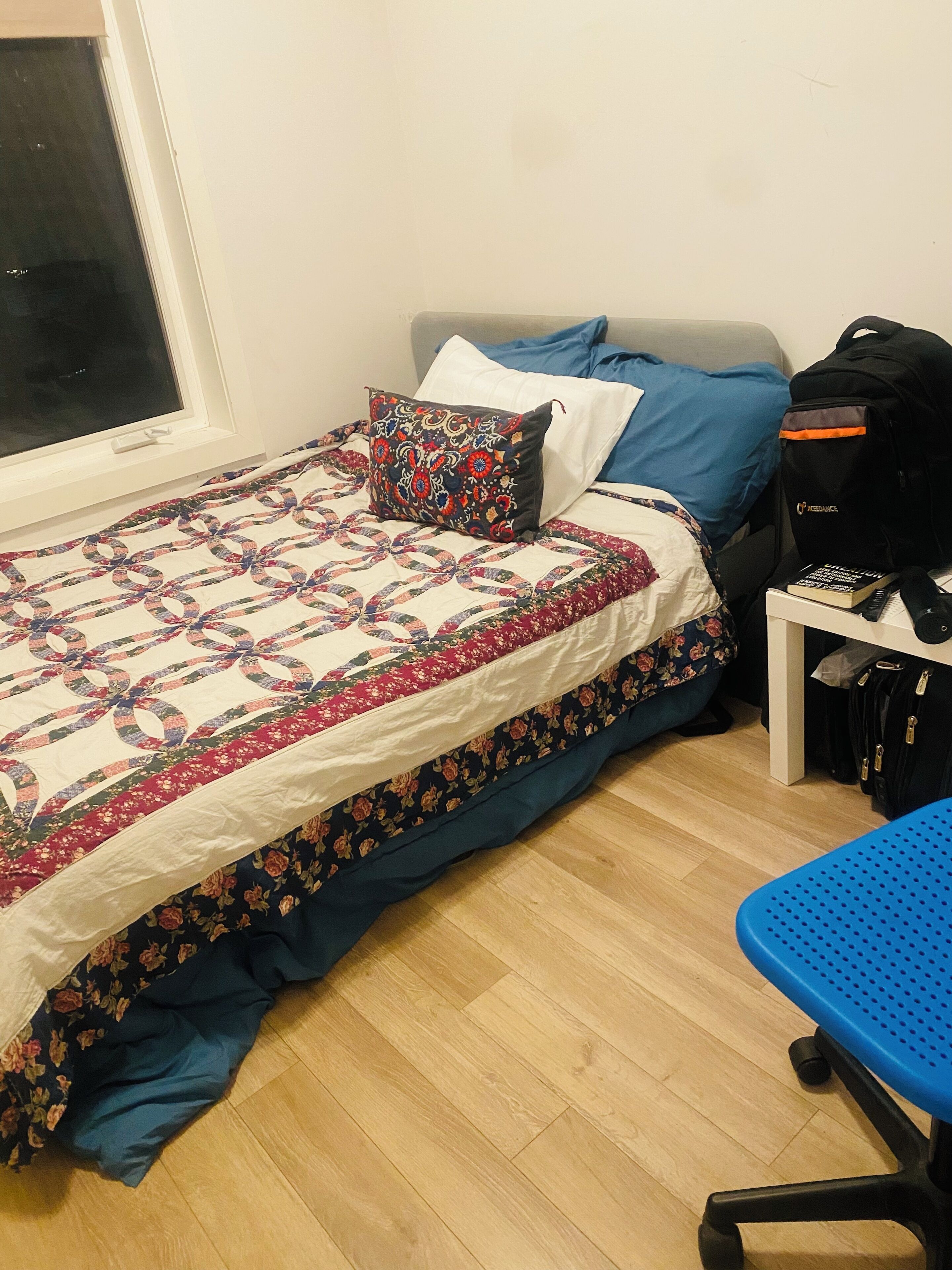 Un dormitorio con una cama, una silla azul, un escritorio con una computadora y una ventana.