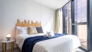 Una camera d'albergo moderna con un letto grande, un comodino con una lampada e vista attraverso un'ampia finestra.