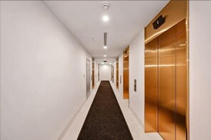 A long, narrow hallway with a carpeted floor, white walls, and a gold elevator on the right. - lvl35 Uno Melbourne CBD with City View (Melbourne)