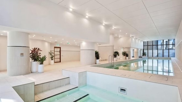 Una piscina interna moderna con barriera in vetro, un'area reception con una porta e piante in vaso.