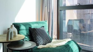 Un divano verde con un cuscino decorato, un tavolino rotondo con due vasi e una coperta in pelliccia.
