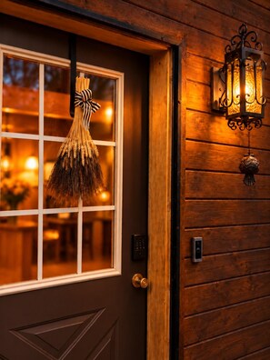 A wooden door with a window, a doorbell, and a wall-mounted light fixture. - Sunset-View Western A-Frame Cabin  Fire Pit & Fenced Yard (Show Low)