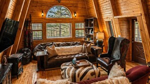 Ein gemütlicher, holzgetäfelter Innenraum mit hohen Decken, einem Kamin, einem Ledersofa, einem roten Sessel und einer Kristallleuchtre.