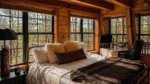 Ein Schlafzimmer einer Holzhütte mit einem Bett, Kissen, einer Decke, einem Schreibtisch und einem Stuhl.