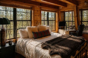 Ein Schlafzimmer einer Holzhütte mit einem Bett, Kissen, einer Decke, einem Schreibtisch und einem Stuhl.