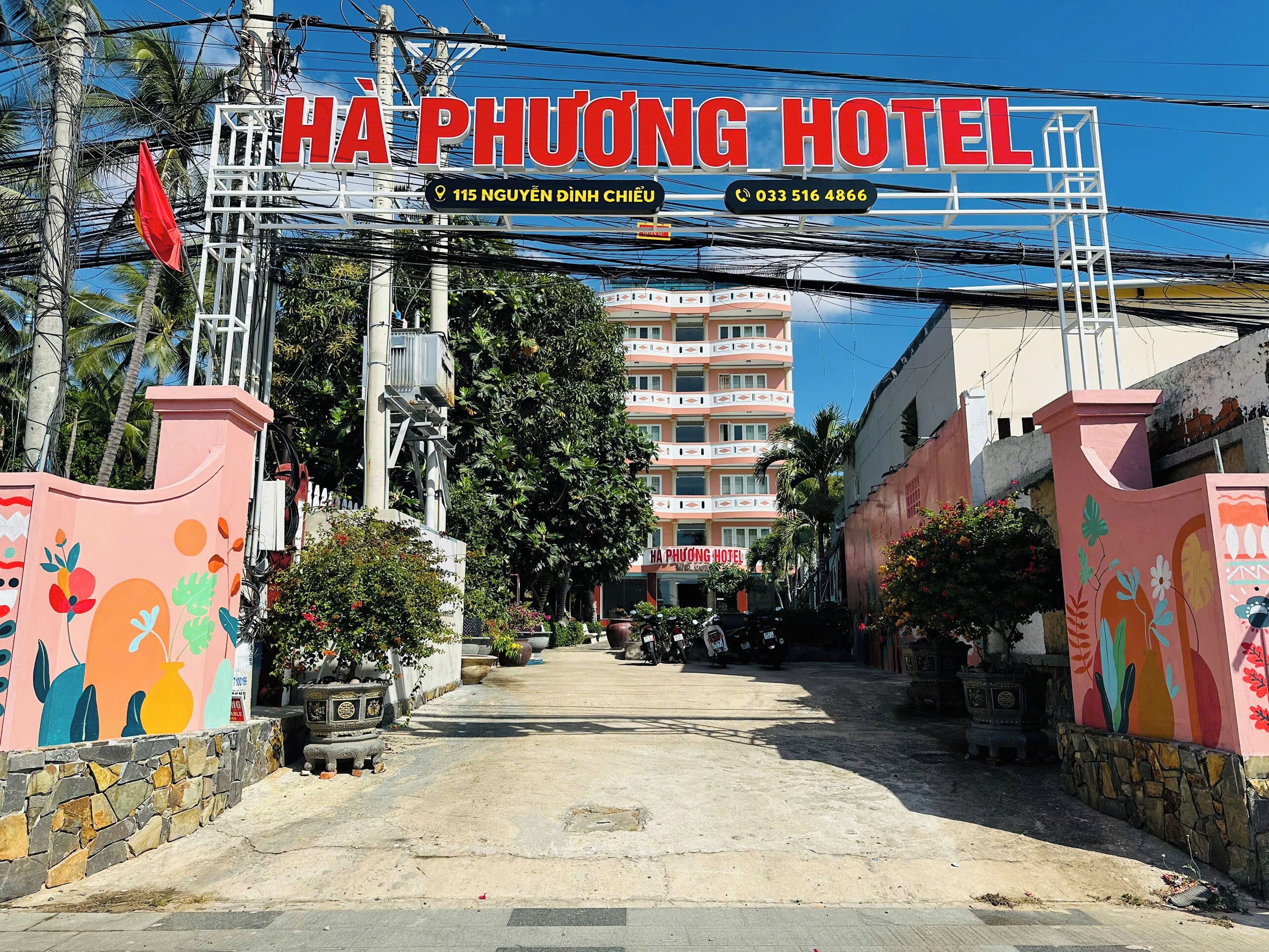 L’entrée de l’hôtel Ha Phuong se distingue par une porte colorée ornée de motifs floraux, un chemin dégagé menant au bâtiment et une enseigne indiquant clairement l’adresse.