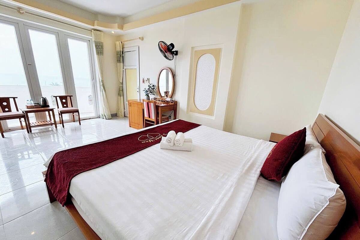Une chambre d’hôtel avec un grand lit, un bureau, une chaise, une coiffeuse avec un miroir et une fenêtre avec des rideaux.
