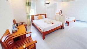 A hotel room with a wooden bed, a wooden table with chairs, a small desk, and a window with curtains.