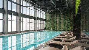 Una piscina interior con agua cristalina, ventanas amplias y una pared verde con jardines verticales.