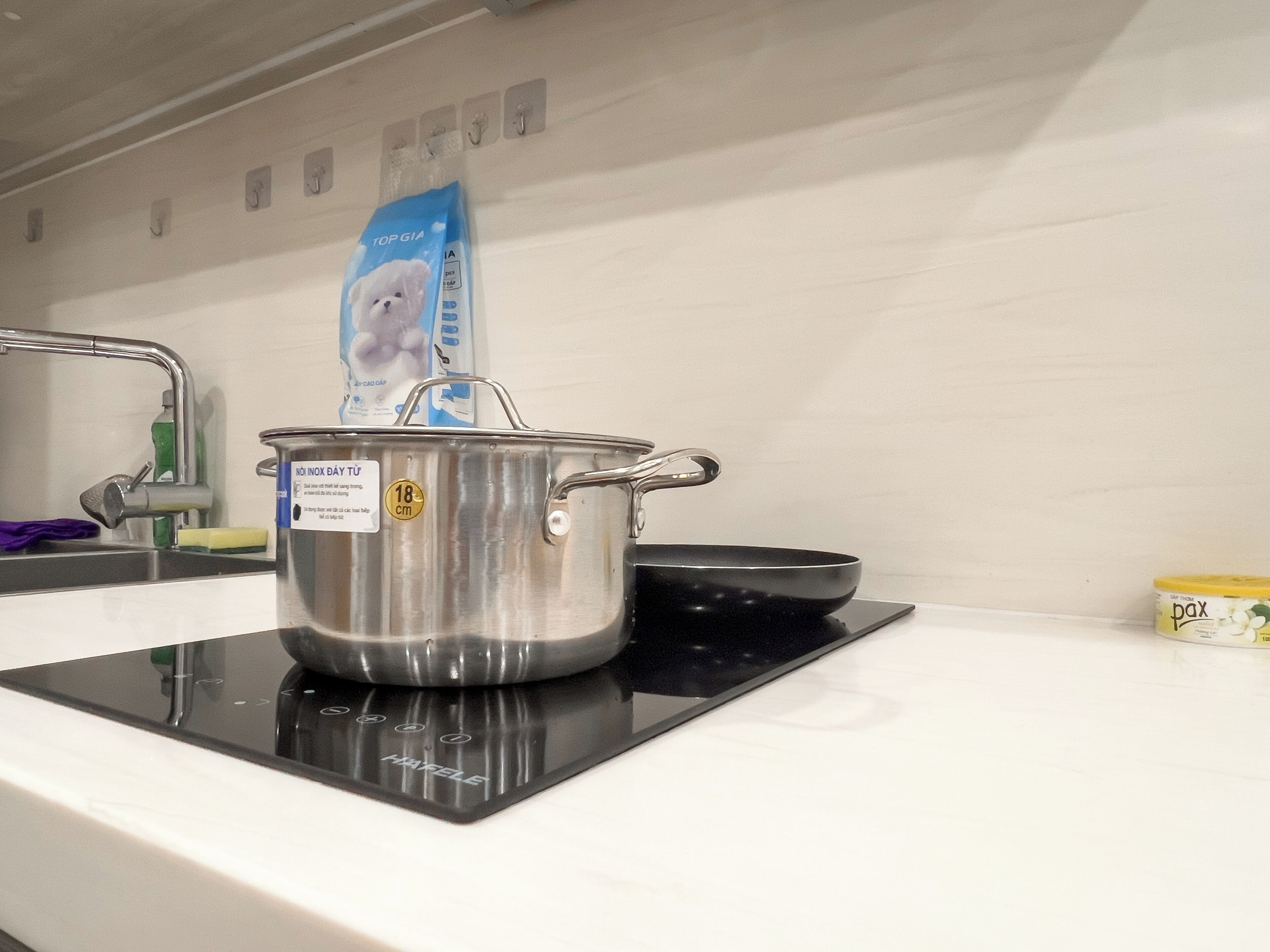 A kitchen with a stove, a pot, a bottle of detergent, and a container of food.