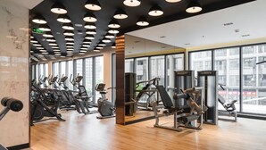 Un gimnasio con máquinas de cardio, zonas de pesas y amplios ventanales con vistas a la ciudad.