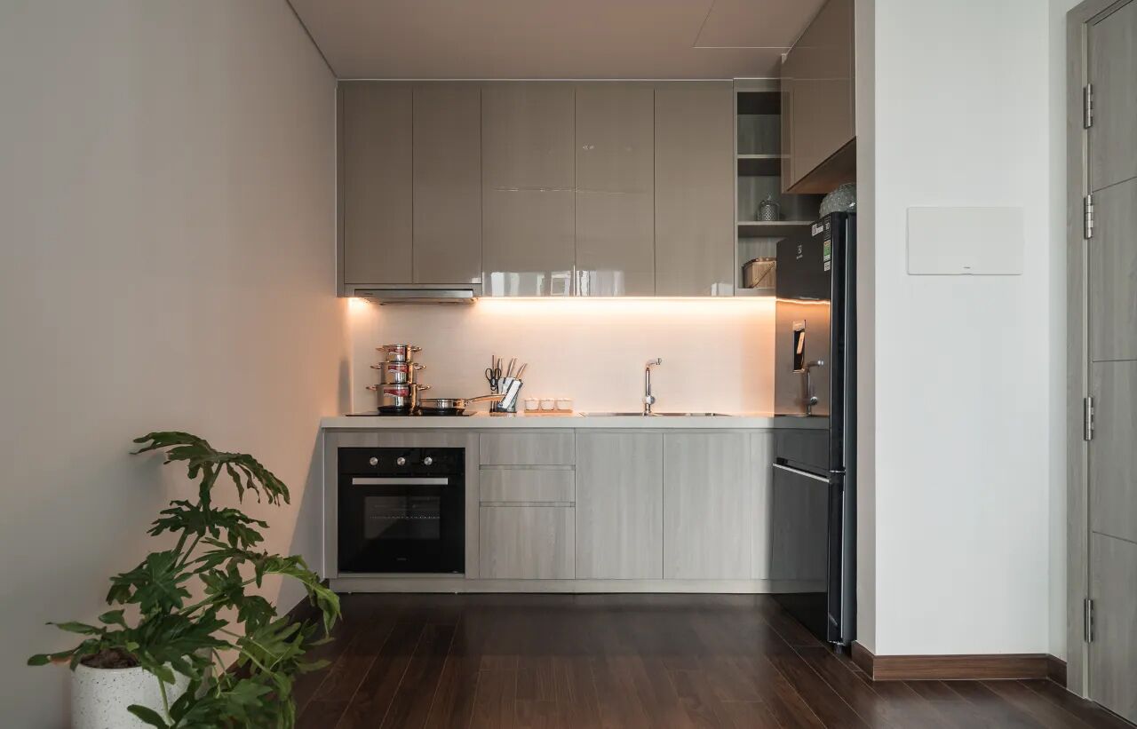 A modern kitchen with grey cabinets, a built-in oven, and a stainless steel refrigerator.