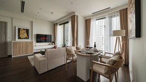 Un moderno salón con sofá, mesa de comedor y sillas. Hay un televisor de pantalla plana montado en la pared y una ventana con cortinas.