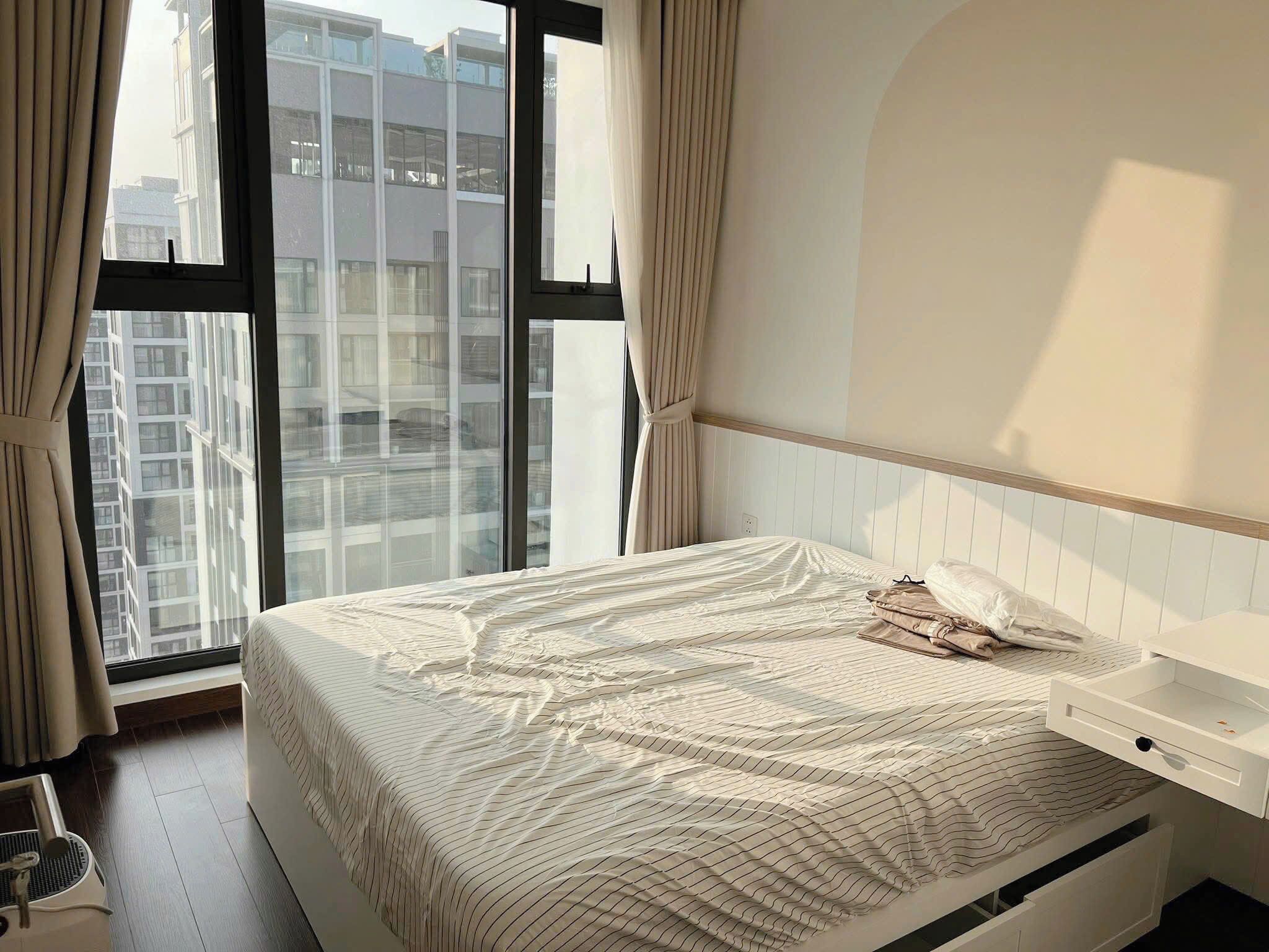 A bedroom with a large window, a bed with a striped bedspread, a bedside table, and a white headboard.