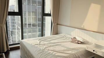 A bedroom with a large window, a bed with a striped bedspread, a bedside table, and a white headboard.