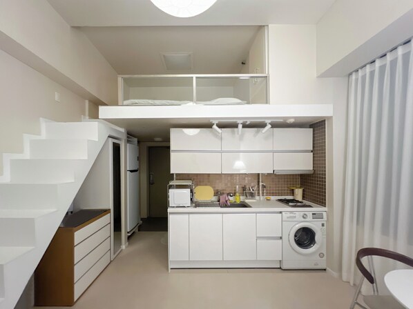 A compact kitchen with a built-in washing machine, a small dining area, and a staircase leading to a loft bedroom.