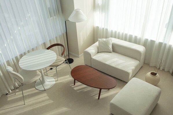 A modern living room with a white sofa, a round coffee table, a white armchair, and a floor lamp.