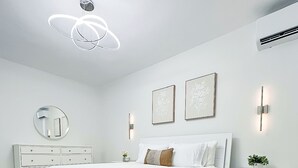 Ein modernes Schlafzimmer mit einem großen Bett, einem Schminktisch, einem Nachttisch, einem Spiegel und Wandleuchten.
