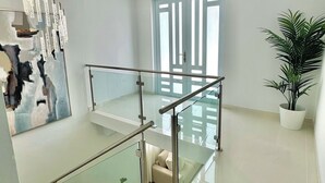 Ein modernes Interieur mit einer Wendeltreppe aus Glasgeländer, einem großen abstrakten Gemälde und einem Topfpflanze.