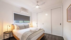 Quarto com cama, luminária de cabeceira, ventoinha no teto, aparelho de ar condicionado e guarda-roupa.