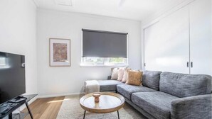 Uma sala de estar moderna com um sofá cinzento, uma televisão de tela plana, uma mesa de centro e um quadro na parede.