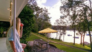 Une terrasse avec une table et des chaises, un parasol jaune et une vue sur un lac où naviguent des bateaux.