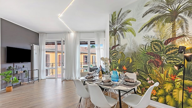 A dining area with a table set for four, white chairs, and a large tropical mural on the wall.