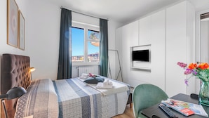 A hotel room with a large bed, a desk with a chair, a TV, and a window with curtains.